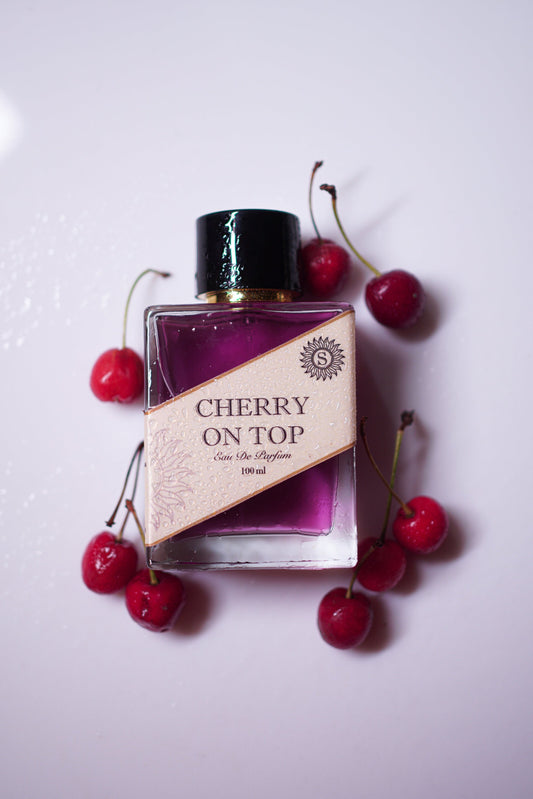 Perfume bottle labeled 'Cherry on Top' surrounded by cherries on a light background